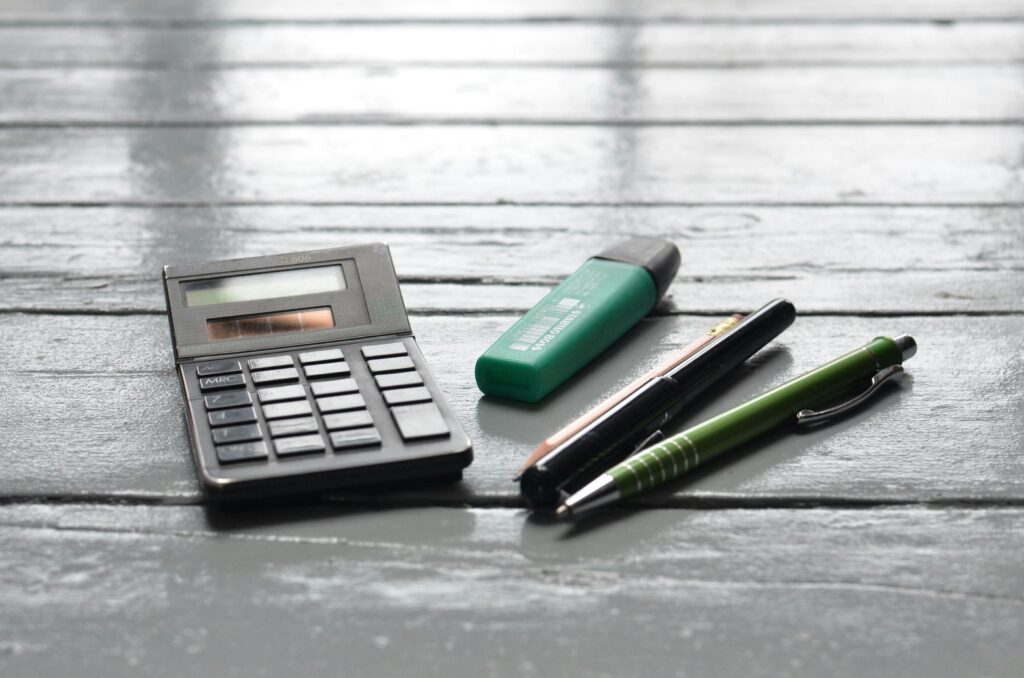 A calculator and pens placed on a wooden desk, ideal for office or educational themes.